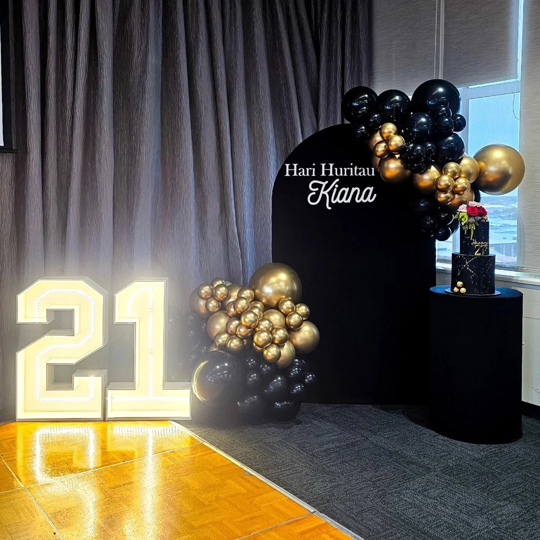 21st backdrop with light-up 21 numbers, black and gold balloons and a personalised arch board
