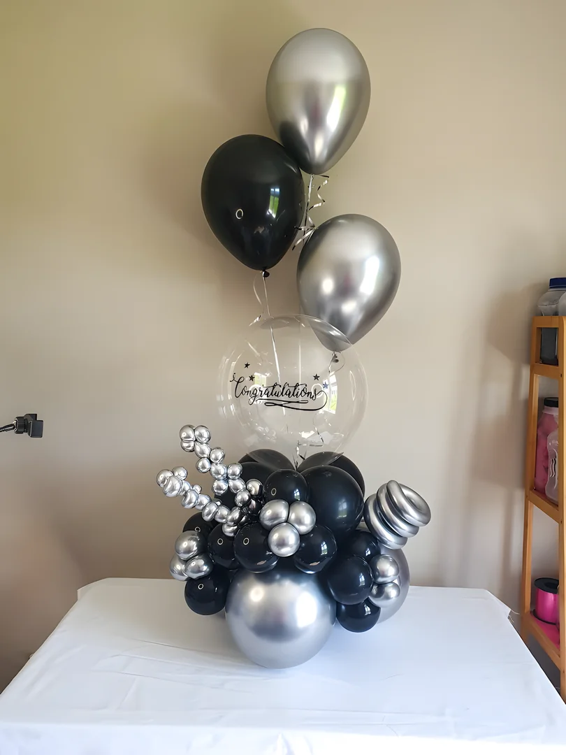 Clear bubble balloon with Congratulations vinyl text on a black and silver balloon base, with black and silver helium balloons above