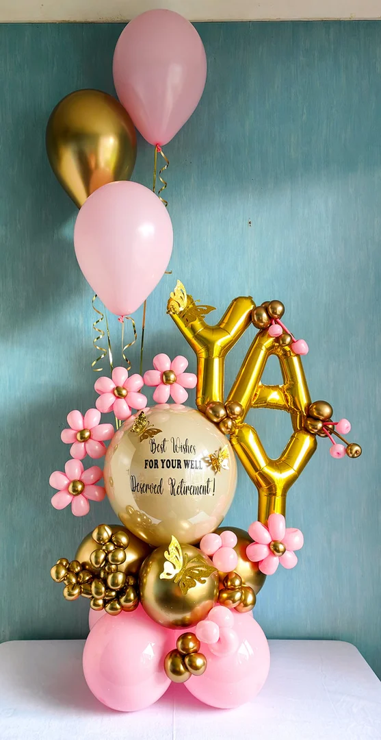 Gold YAY foil letter balloons beside a personalised retirement bubble balloon with pink balloon flowers on a pink and gold balloon base