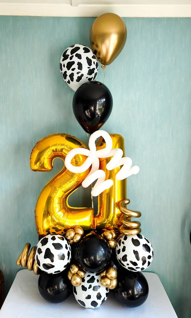 Gold 21 foil numbers with a white twisted balloon bow, cow print balloons and black and gold helium balloons