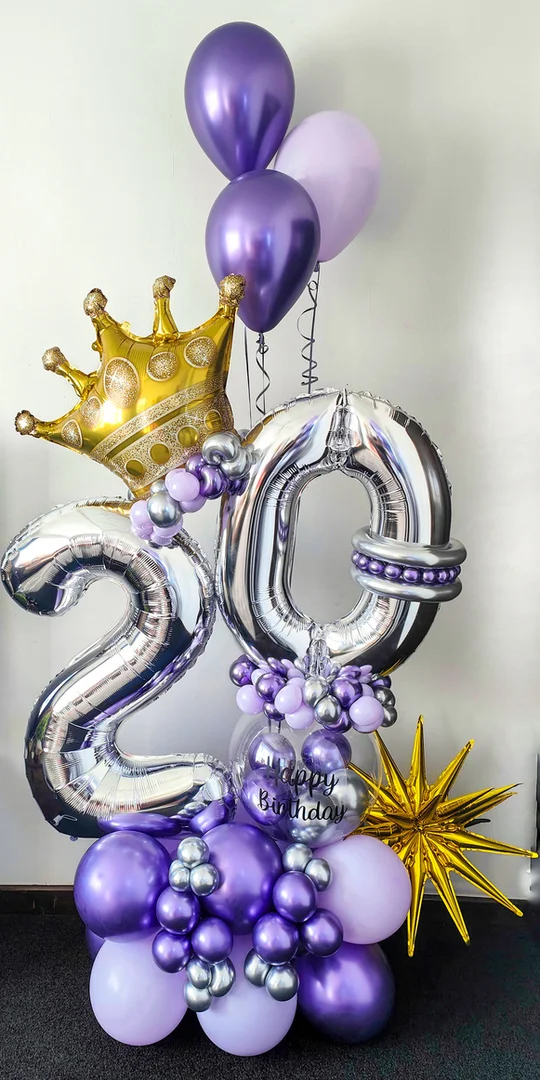 Silver 20 foil numbers with a gold crown topper, a Happy Birthday bubble balloon, a gold starburst and purple helium balloons on a purple and silver base