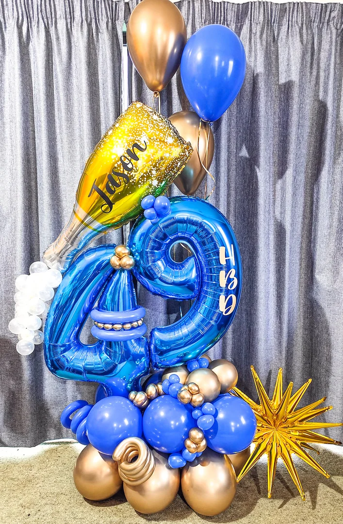 Blue 49 foil number balloons with a personalised gold champagne bottle balloon and a gold starburst on a blue and gold balloon base