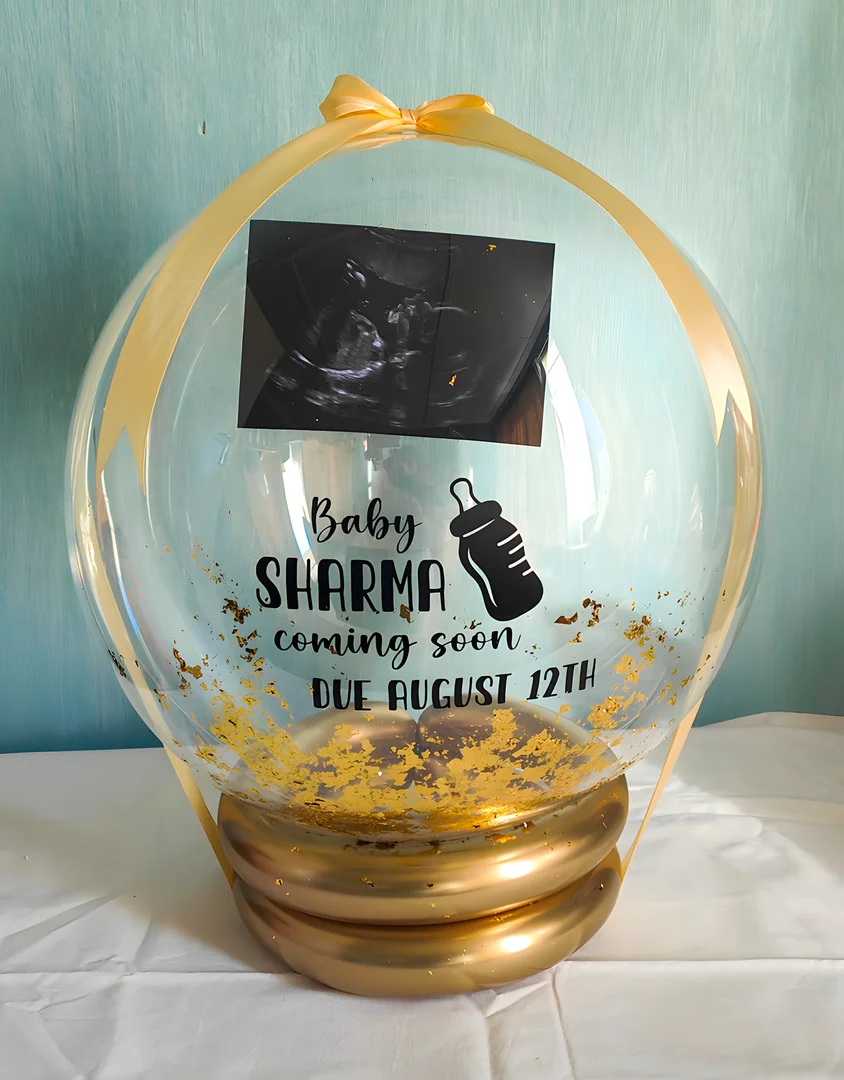 Clear bubble balloon with a printed baby scan photo, gold leaf flakes, a gold ribbon bow and a gold balloon ring base