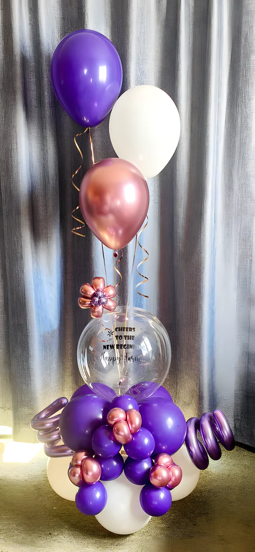 Clear bubble balloon reading Cheers to the New Beginnings on a purple and rose gold balloon base with purple, white and rose gold helium balloons