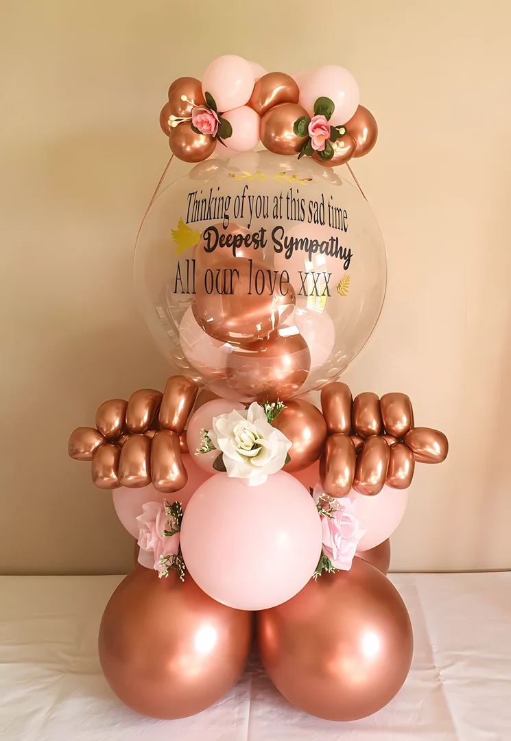 Clear sympathy bubble balloon filled with rose gold balloons, decorated with artificial roses and rose gold and blush balloons