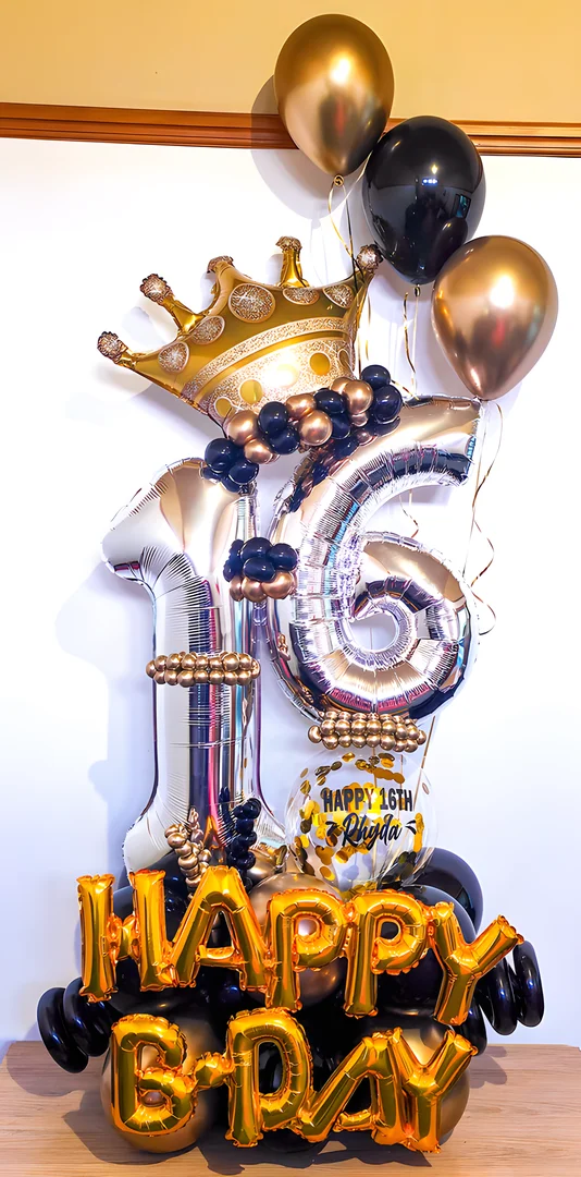 Silver 16 foil numbers with a gold crown topper, a Happy 16th bubble balloon and gold Happy B-Day letter balloons on a black and gold base