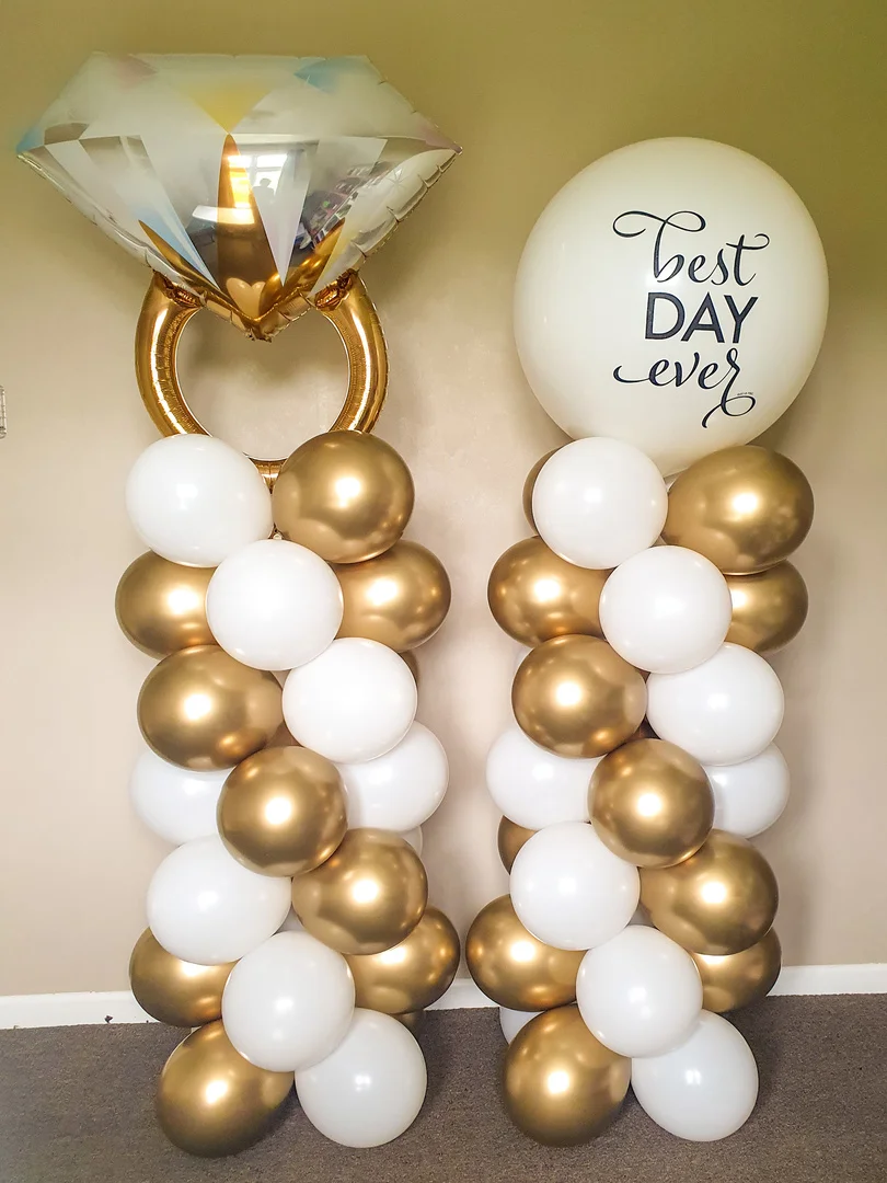 Two gold and white balloon columns, one topped with a diamond ring foil balloon and one with a Best Day Ever balloon